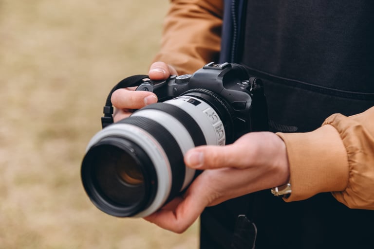 black and white dslr camera in hands, large long lens, young caucasian man photographer at work outdoors in sunny summer day