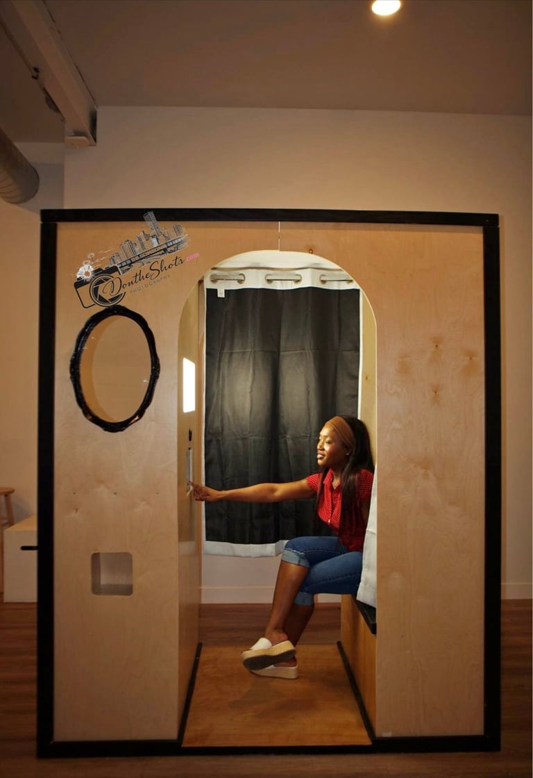 Woman in red shirt posing inside a framed photo booth setup with black curtain backdrop and oval ring prop on wall