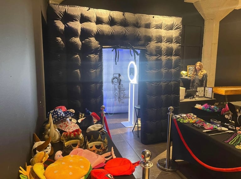 Modern event space with black padded wall backdrop, neon sign, party decorations, and tables with red ribbon barriers