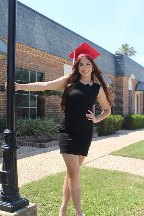 Young woman in black dress and red graduation cap posing outside brick school building
