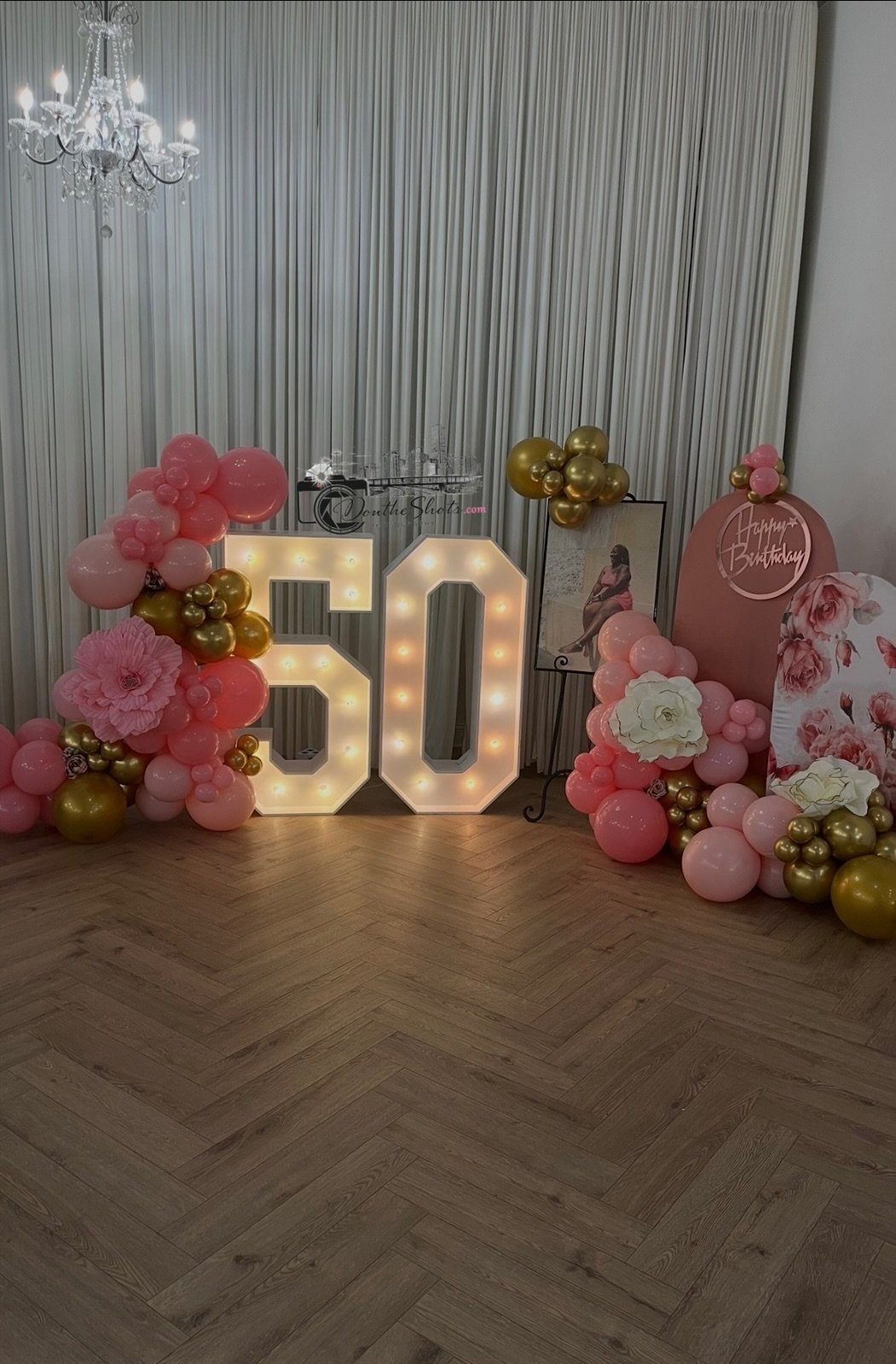 Illuminated number 50 display surrounded by pink and gold balloons and flowers at a birthday celebration venue
