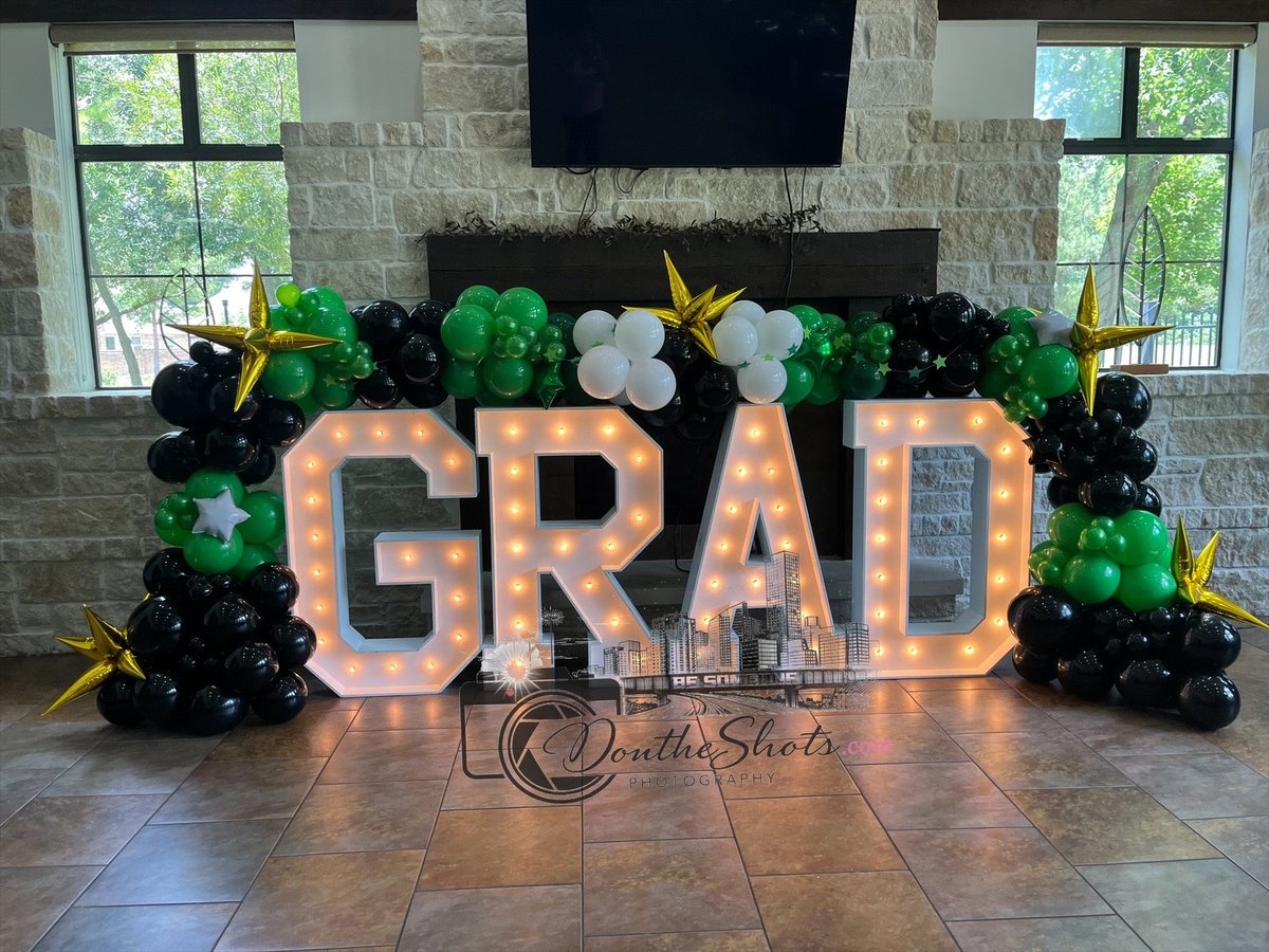 Large illuminated GRAD sign with green and black balloon decorations in an indoor venue