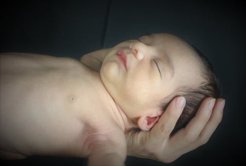 Newborn baby sleeping peacefully, cradled in gentle hands against a dark background