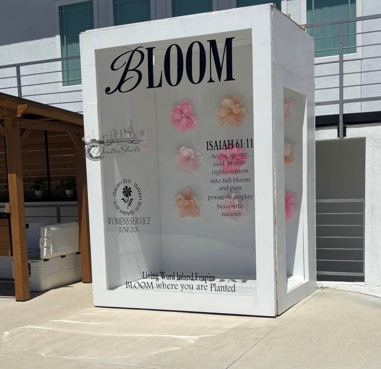 White BLOOM installation booth with pink and peach flowers and scripture text on a patio