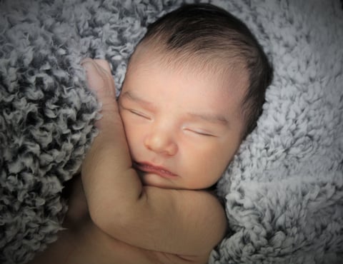 Sleeping newborn baby resting on a soft gray textured blanket with eyes closed
