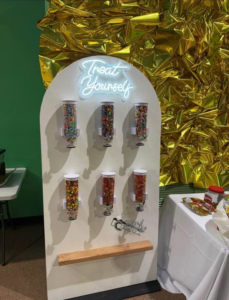 White self-serve candy display with Treat Yourself neon sign, six glass jars filled with colorful candies, and wooden scoop against gold foil backdrop