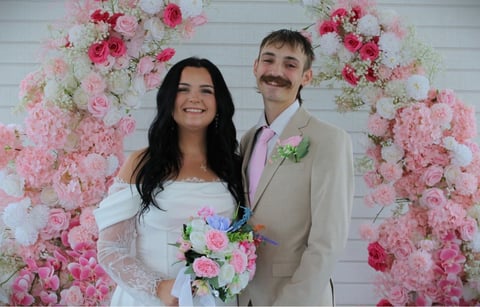 Bride and groom smiling in front of pink and white floral wedding backdrop