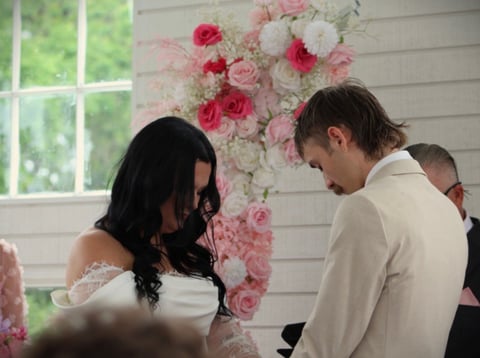 Couple exchanging vows with pink and white floral backdrop