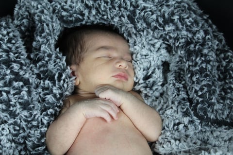 Newborn baby sleeping peacefully on gray textured blanket, shirtless with hand near face