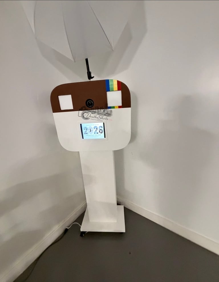 White cardboard craft figure with brown head, antenna, and colorful stripes standing in corner against white wall
