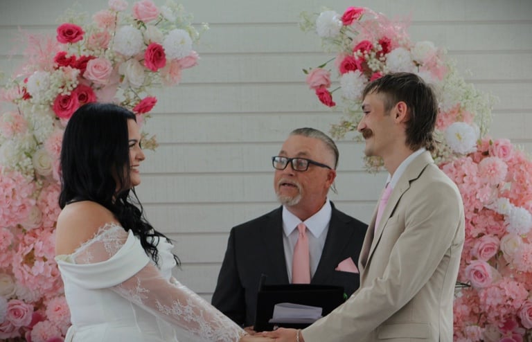 Wedding ceremony with bride and groom facing officiant beneath floral arch