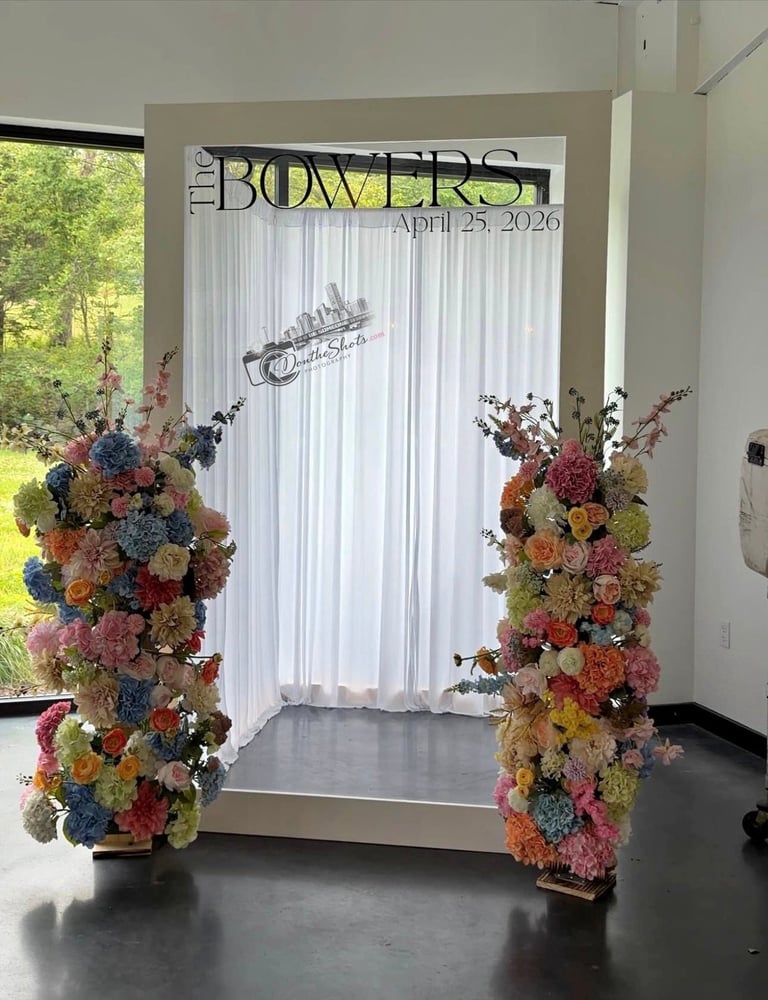Wedding ceremony backdrop with colorful floral arrangements on both sides, white curtains, and Bowers signage