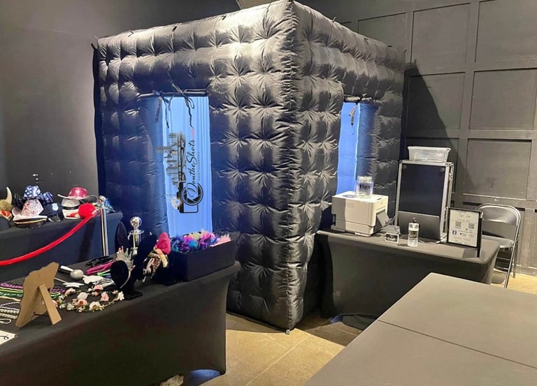 Inflatable black photo booth with blue doors inside a studio space with makeup table and computer workstation