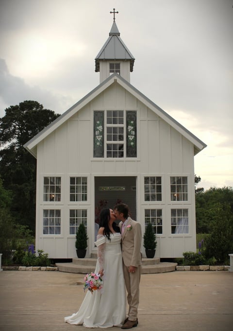 Bride and groom kissing in front of white chapel on wedding day