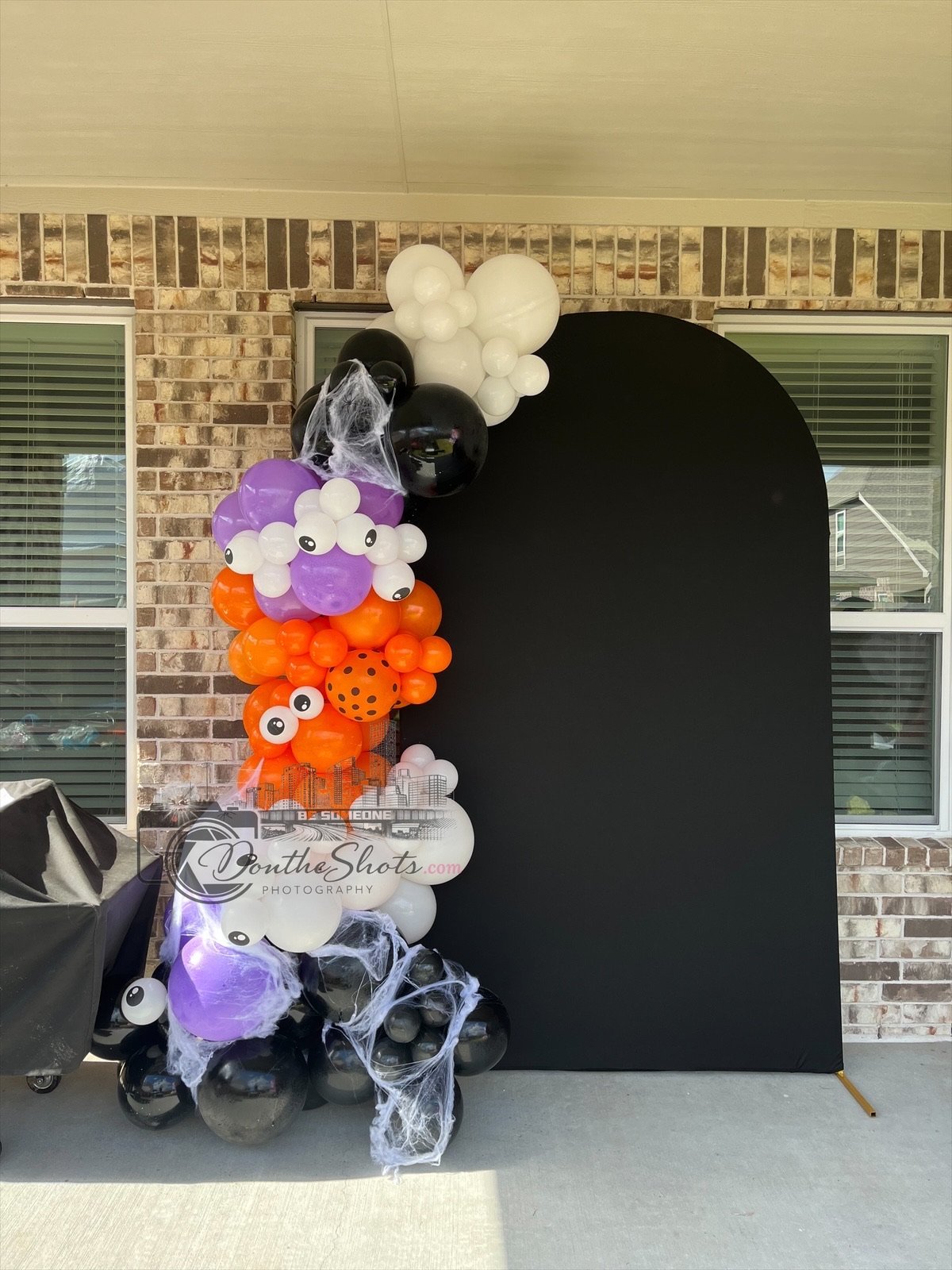 Halloween photo booth backdrop with black arch decorated with white, purple, and orange pom-poms