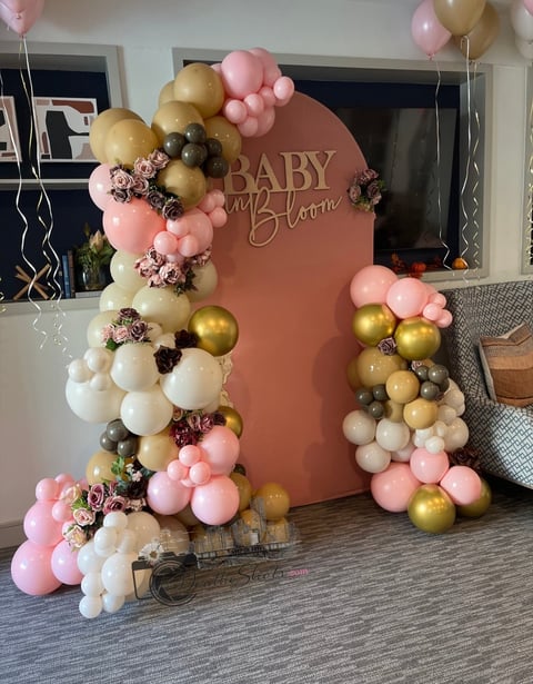 Baby shower photo backdrop with terracotta arch displaying BABY and Bloom text, decorated with pink, gold, white, and burgundy balloons arranged in garland clusters