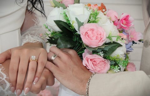 Bride and groom displaying wedding rings with pink and white bouquet