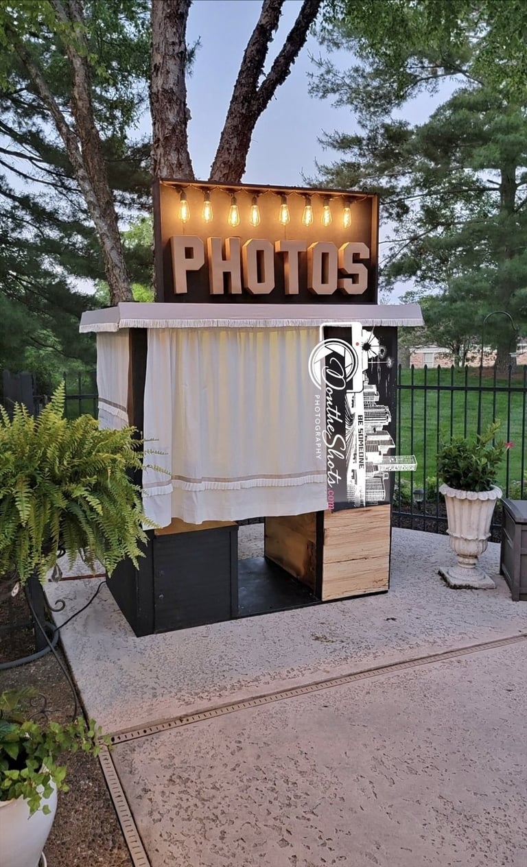Vintage-style photo booth with illuminated PHOTOS sign, white curtain, and wooden door