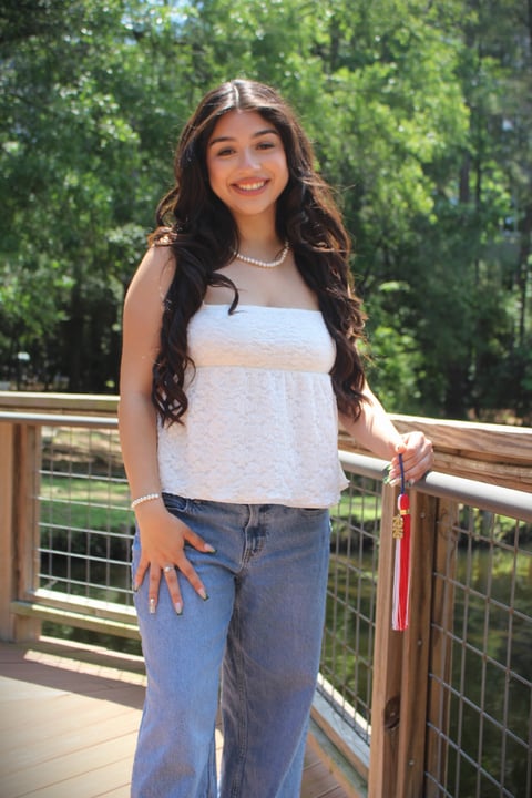Young woman smiling on a wooden deck with trees in background, wearing white top and blue jeans