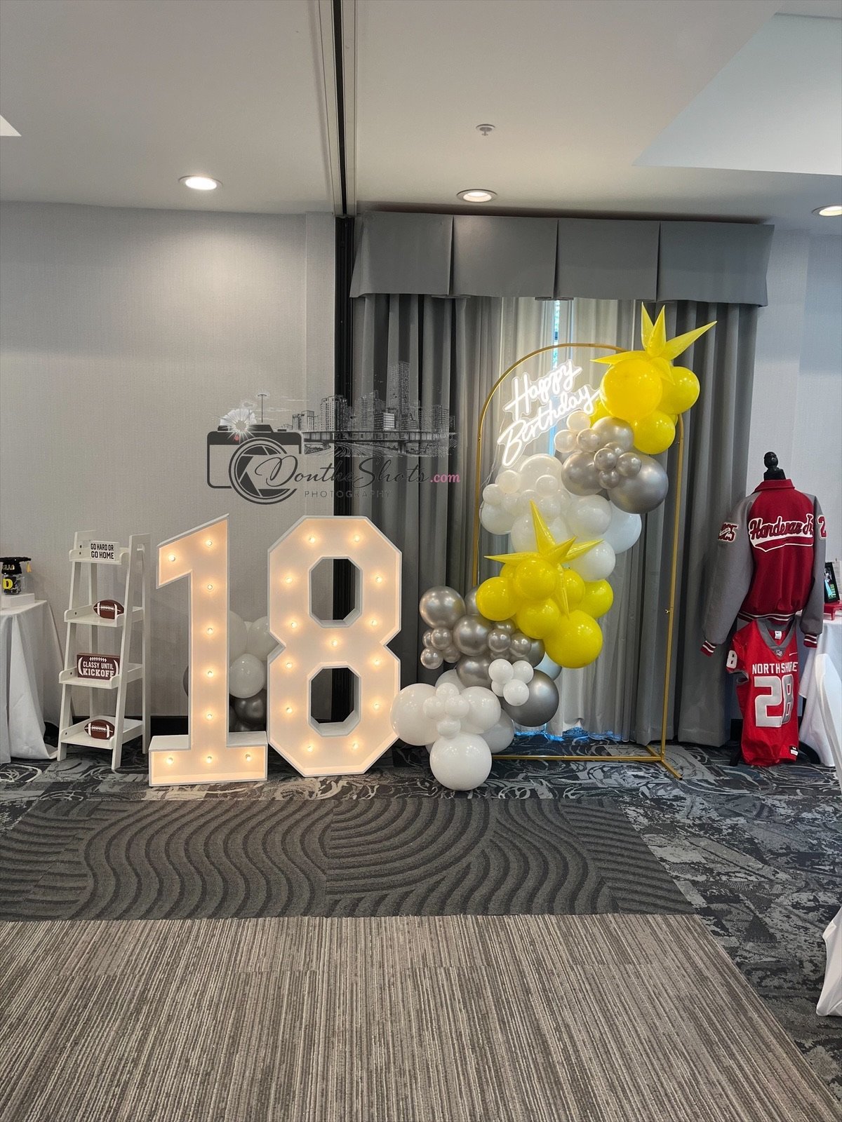 Large illuminated 18 number display with white and silver balloons and yellow star decorations