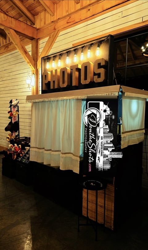 Illuminated vintage-style photo booth with Adonis sign, cream curtains, and wooden frame inside a rustic building