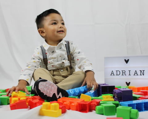 Toddler boy named Adrian playing with colorful building blocks, wearing suspenders and patterned shirt