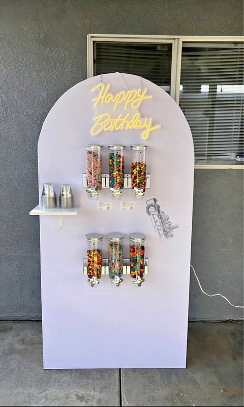 Large white arch-shaped birthday display with yellow neon Happy Birthday sign and shelves holding colorful candy dispensers