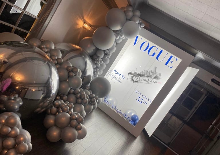 Vogue magazine displayed with metallic bronze and silver decorative balloons and warm string lights on white tile floor