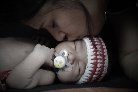 Infant sleeping while holding a pacifier, wearing a red and white striped hat