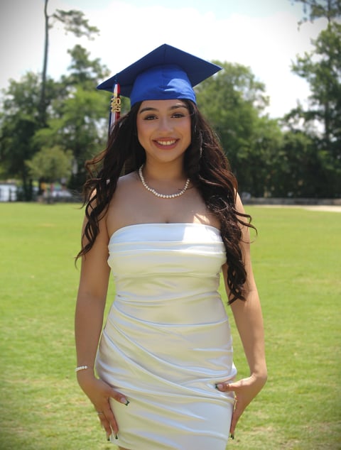 Woman in blue graduation cap and white striped dress smiling outdoors on a grass field